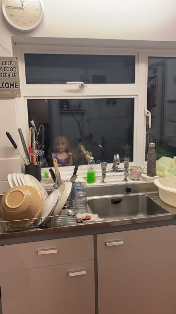 A kitchen scene with a creepy doll appearing outside the window.