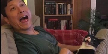 Man and cat bonding on couch, woman feels like third wheel.