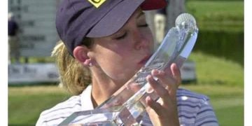 Woman kisses bizarrely shaped golf trophy with a smirk.