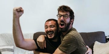 Two friends celebrating on a couch as one hits it off with their crush.