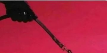 A sub sandwich humorously strapped with a belt on pink background.