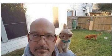 Man taking a selfie with a kitten sitting on his shoulder.
