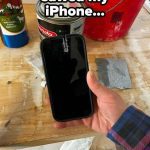 Hand holding damaged iPhone with saw cut in a workshop setting.