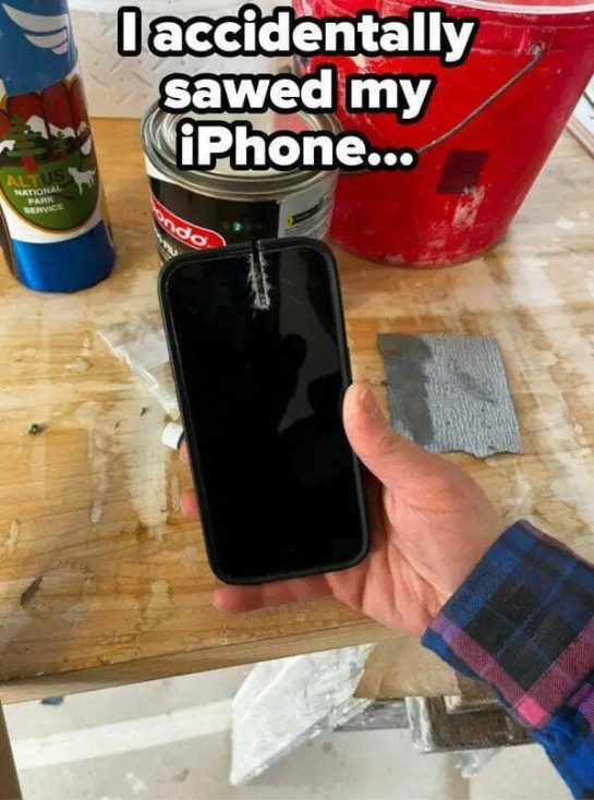 Hand holding damaged iPhone with saw cut in a workshop setting.