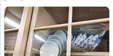 A stack of plates precariously balanced behind a glass cabinet door.
