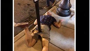 Person humorously lying under a street pole, epic fail moment.
