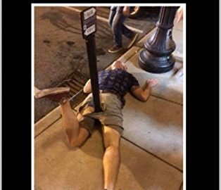 Person humorously lying under a street pole, epic fail moment.