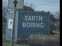 Blue container with "Earth Boring" graffiti under a road sign.