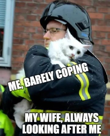 Firefighter holding a white cat, with text "Me, Barely Coping"