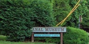 Overgrown hedge covers part of the canal museum sign, creating funny wordplay.