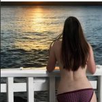 Person admiring a sunset over water from a balcony.