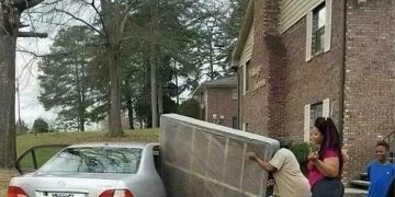 Three people struggling to fit a mattress into a car.