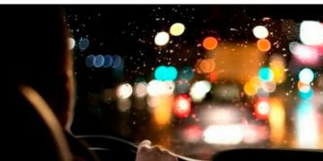Driver navigating a rainy, blurry road at night with colorful lights.