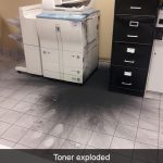 Office printer with exploded toner creating a messy black spill.