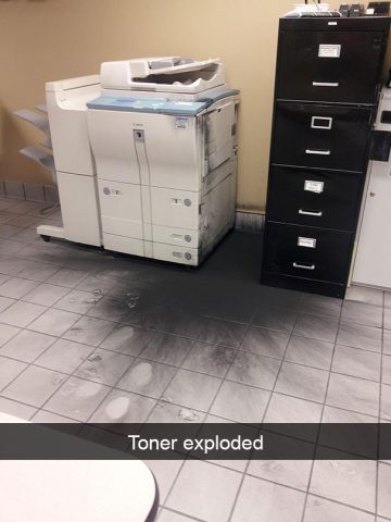 Office printer with exploded toner creating a messy black spill.