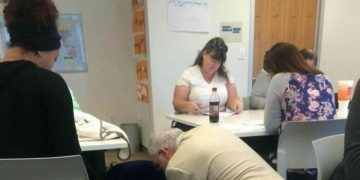 Professor kneeling to feed a baby in a classroom setting.