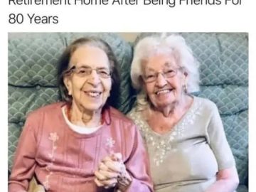 Two elderly women smiling, holding hands in a retirement home.