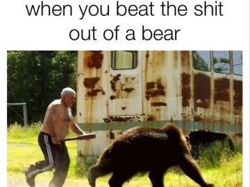 Man confidently chases a bear with a stick in front of a trailer.