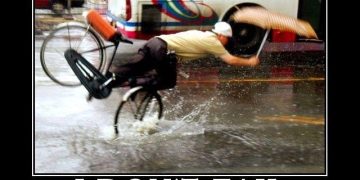 Man hilariously falling off a bike in the rain with an umbrella.