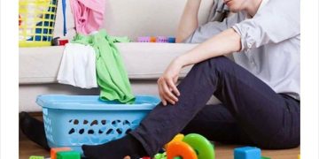 Exhausted man surrounded by laundry and toys after a lazy day.