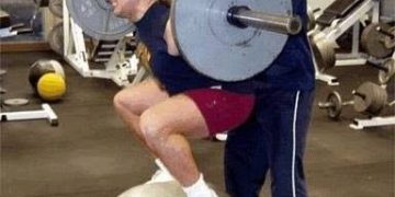 Man squatting on a gym ball with weights, about to fall