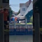A large boat tips awkwardly near a waterfront while several people try to guide it back under control.
