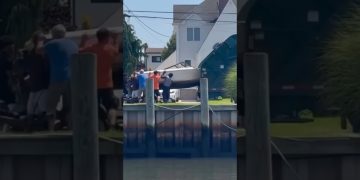 A large boat tips awkwardly near a waterfront while several people try to guide it back under control.
