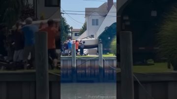 A large boat tips awkwardly near a waterfront while several people try to guide it back under control.