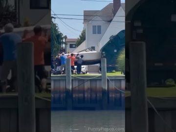 A large boat tips awkwardly near a waterfront while several people try to guide it back under control.