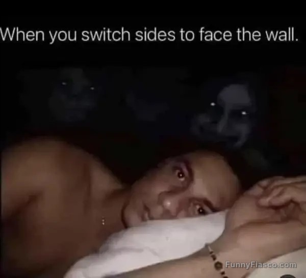 Man in bed wide awake facing wall with creepy shadows.
