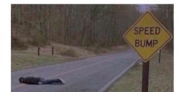 Person lying on road as a speed bump next to sign, dark humor