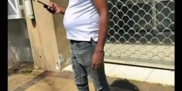 Man with a visible belly standing outside texting on his phone.