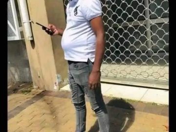 Man with a visible belly standing outside texting on his phone.