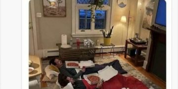 Three friends in sleeping bags with pizza, watching TV.