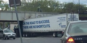 Truck stuck under bridge with sign "No Shortcuts on Road to Success."