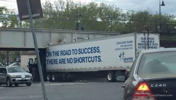 Truck stuck under bridge with sign "No Shortcuts on Road to Success."