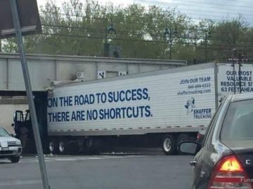 Truck stuck under bridge with sign "No Shortcuts on Road to Success."