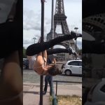 A woman hanging upside down from a street pole near the Eiffel Tower before slipping into an awkward fail.