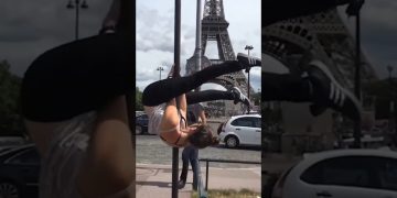 A woman hanging upside down from a street pole near the Eiffel Tower before slipping into an awkward fail.