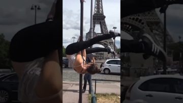 A woman hanging upside down from a street pole near the Eiffel Tower before slipping into an awkward fail.