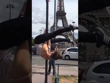 A woman hanging upside down from a street pole near the Eiffel Tower before slipping into an awkward fail.