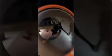 A person tumbles inside a playground spinning tube during a funny park fail.