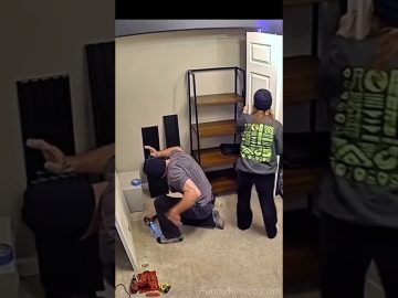 A woman carrying a long white board accidentally bumps into a kneeling man during a DIY shelf project.